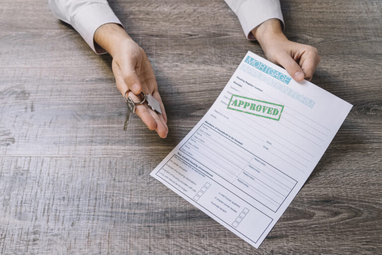 A person holding a mortgage application form and keys on a wooden table.